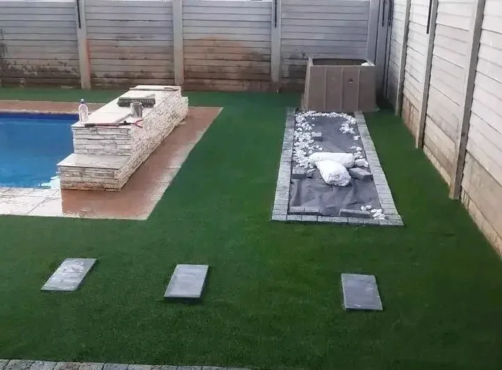 Artificial turf laid around a pool with stone-clad walling, stepping stones and a pebble bed